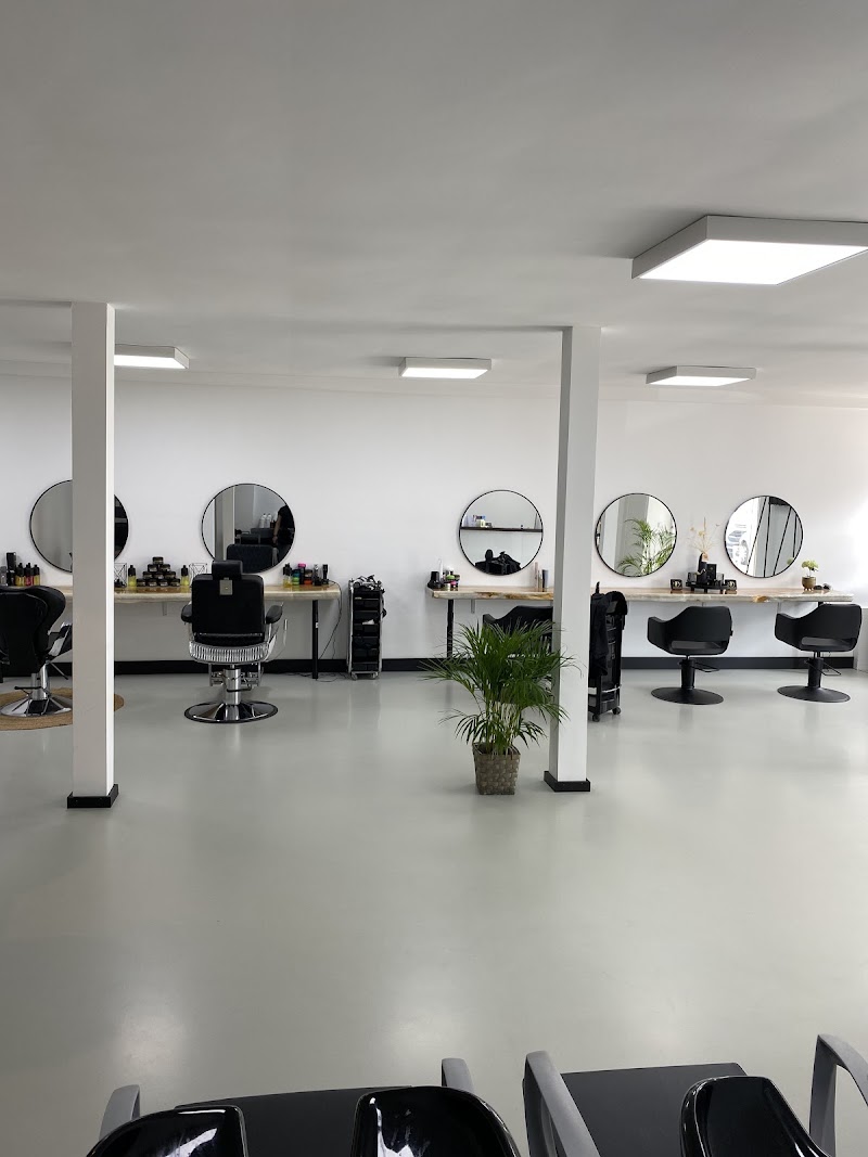 Het interieur van D Hairsalon: witte ruimte met ronde spiegels, moderne kappersstoelen en een klassieke barberstoel.